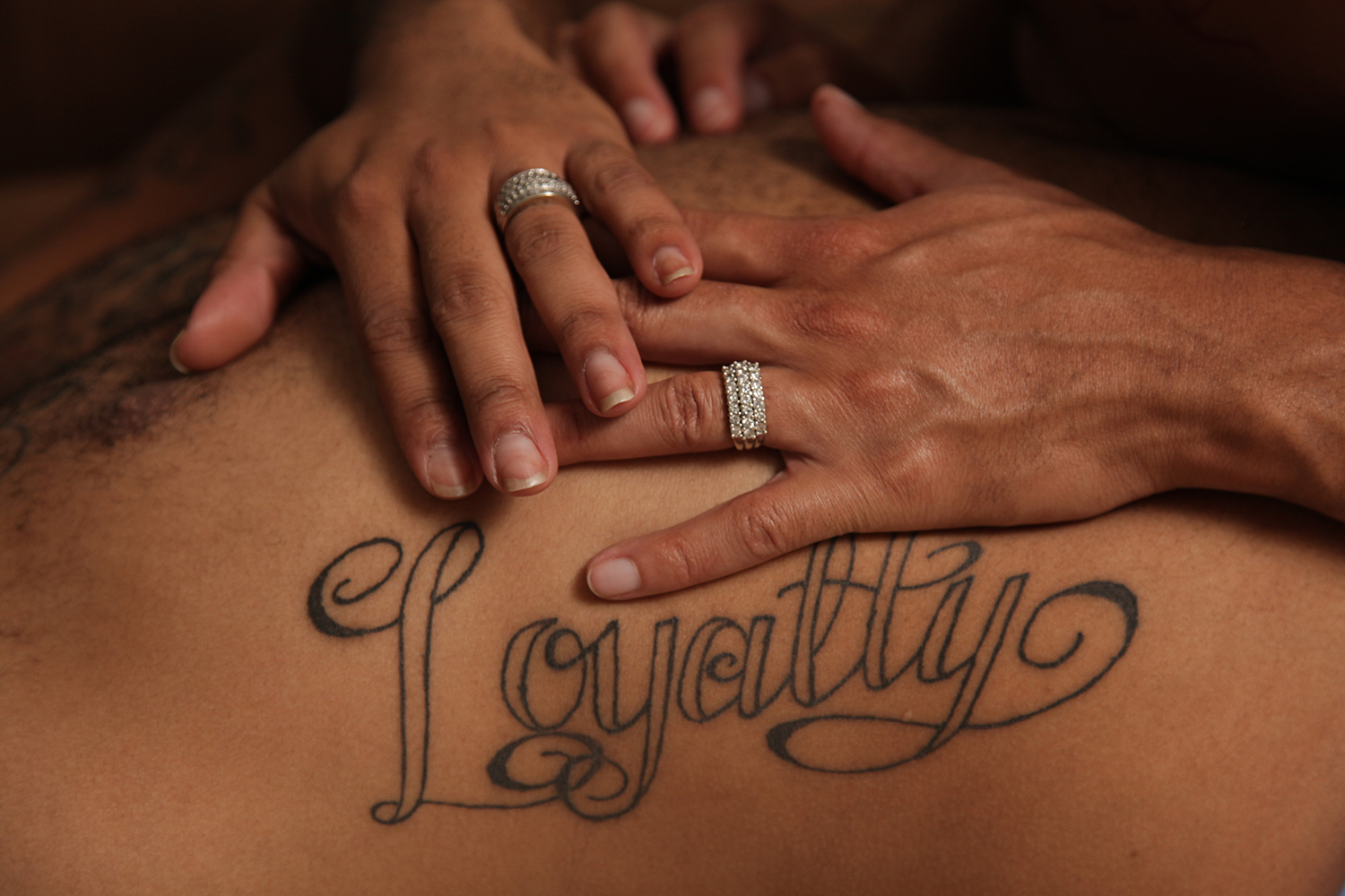 A man's hands on another's back with the tattoo reading "Loyalty" across the spine and shoulder blades.